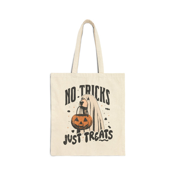 An off-white canvas tote bag with a Halloween graphic that reads 'NO TRICKS JUST TREATS' in black lettering, featuring a cartoon ghost, a pumpkin, and bats.