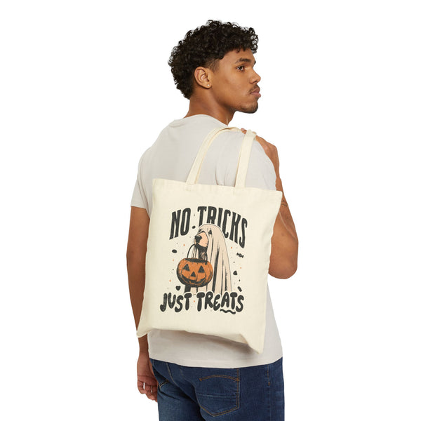 Person holding a tote bag with "No tricks, just treats" graphic of a dog wearing a ghost costume and holding a Halloween pumpkin. 
